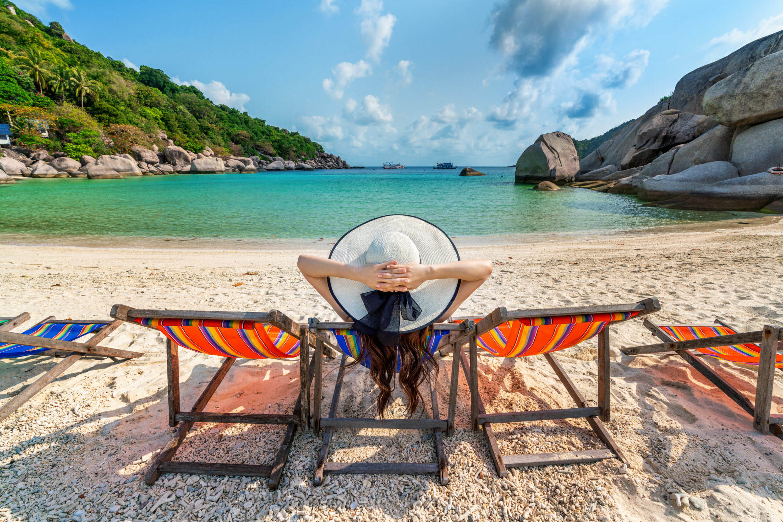 woman with hat sitting on chairs beach in beautiful tropical bea